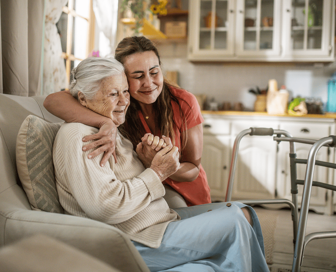 Elderly woman embraced by younger woman, smiling.