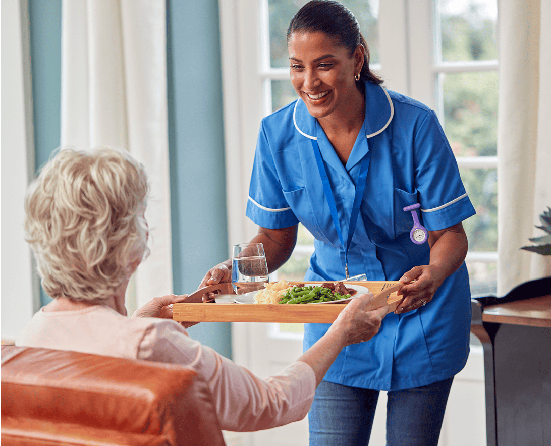 Caregiver serving meal to elderly woman.