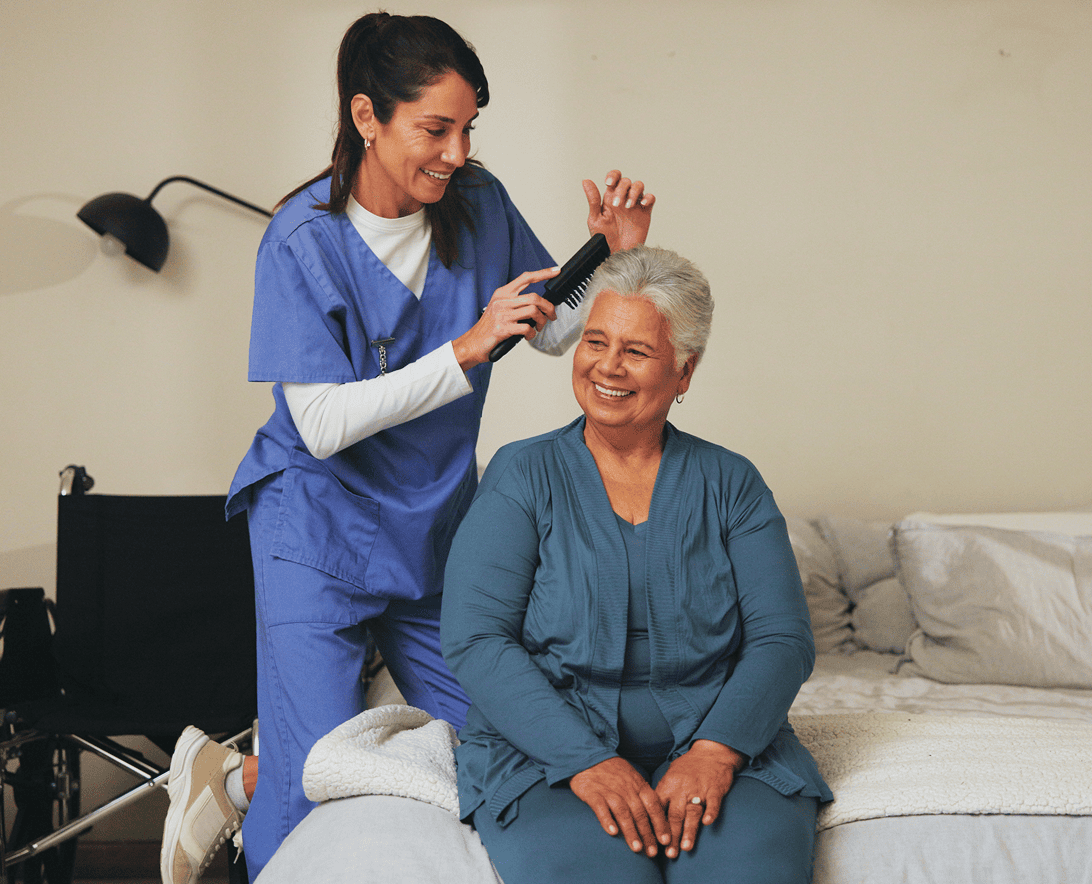 Caregiver brushing elderly woman's hair, smiling together.